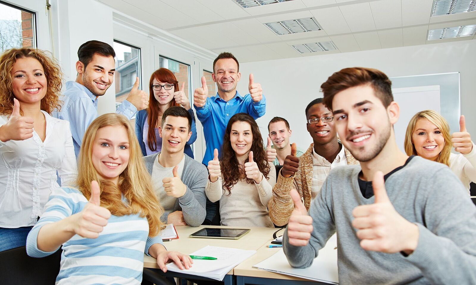 Eine fröhliche Berufsschulklasse sitzt mit einem Lehrer im Klassenzimmer